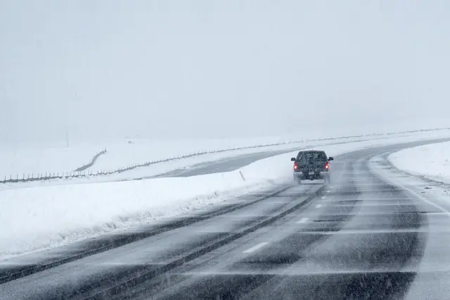 A car drives through heavy snow on an open road in Broomfield, Colorado